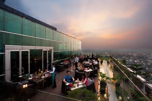 An outdoor dining area with tables and chairs, surrounded by glass walls and potted plants. - Cambridge Hotel Medan (Medan)