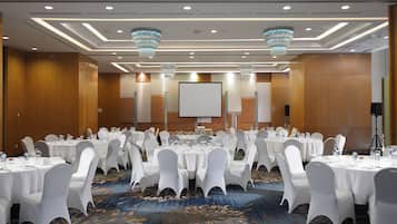 Un salón de conferencias con mesas redondas, sillas blancas y una pantalla grande.