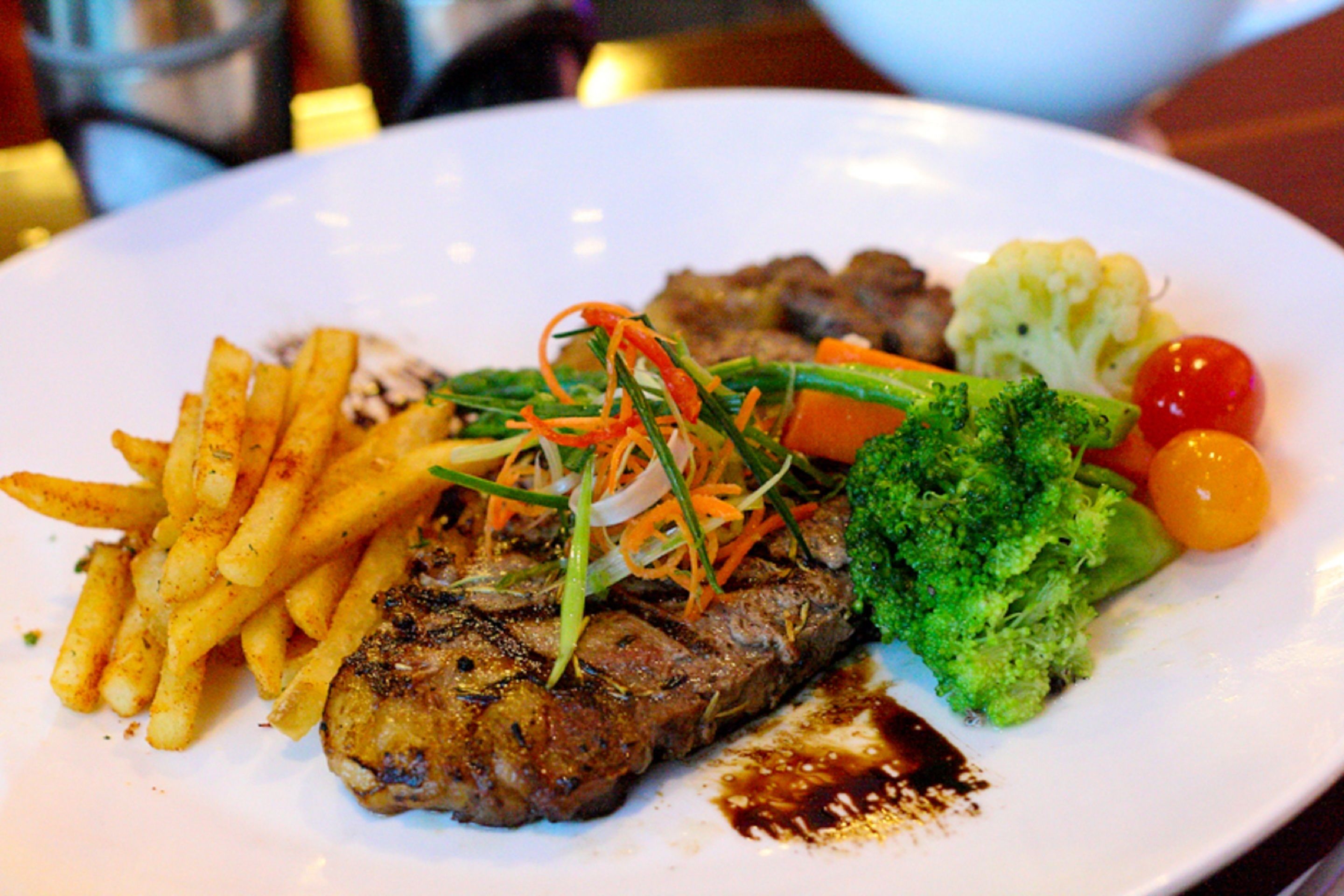 A plate with steak, fries, broccoli, and cherry tomatoes.