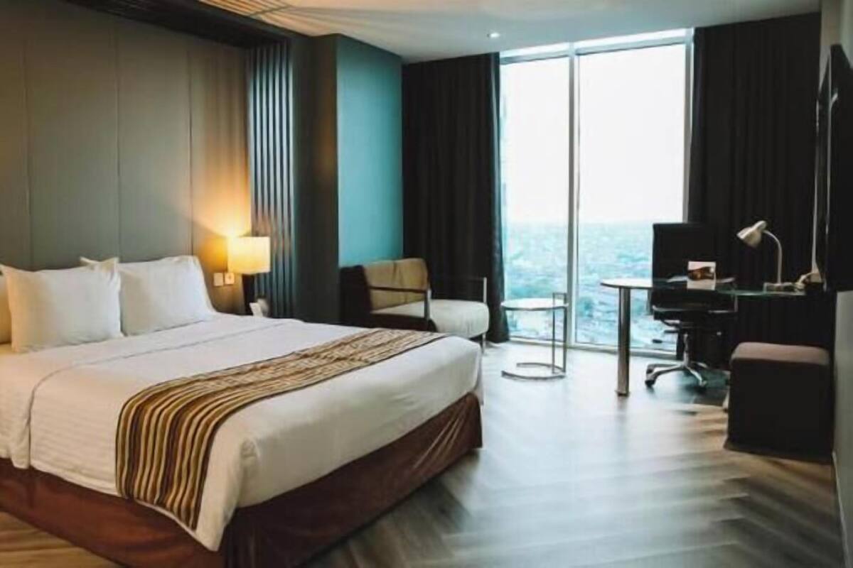A hotel room with a large bed, a desk, a chair, and a view of the city.