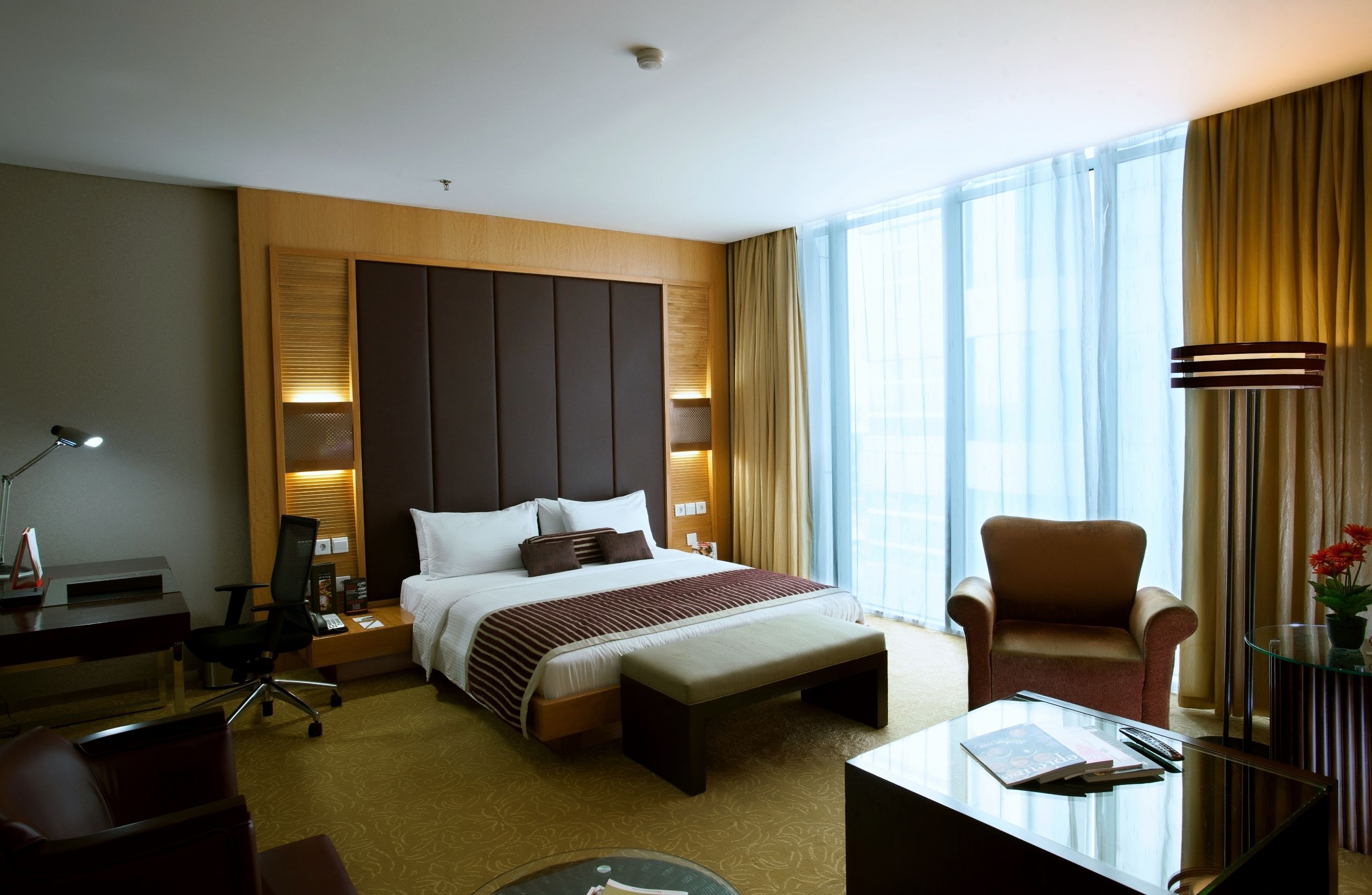 Habitación de hotel con una cama grande, un escritorio con una silla, una mesita, una lámpara y una ventana con cortinas.