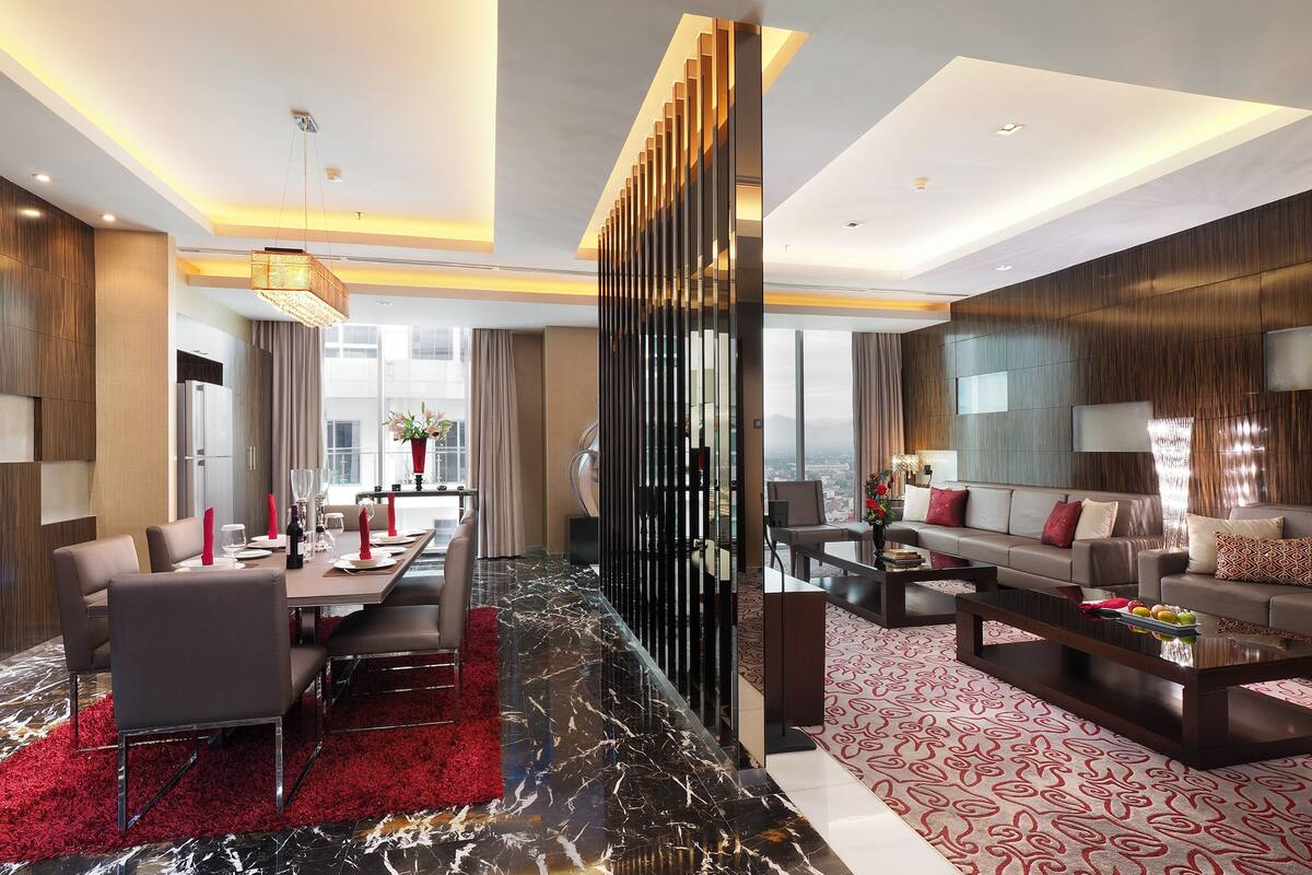A modern hotel lobby with a dining area, a seating area with a sofa and coffee table, and a decorative wall panel.