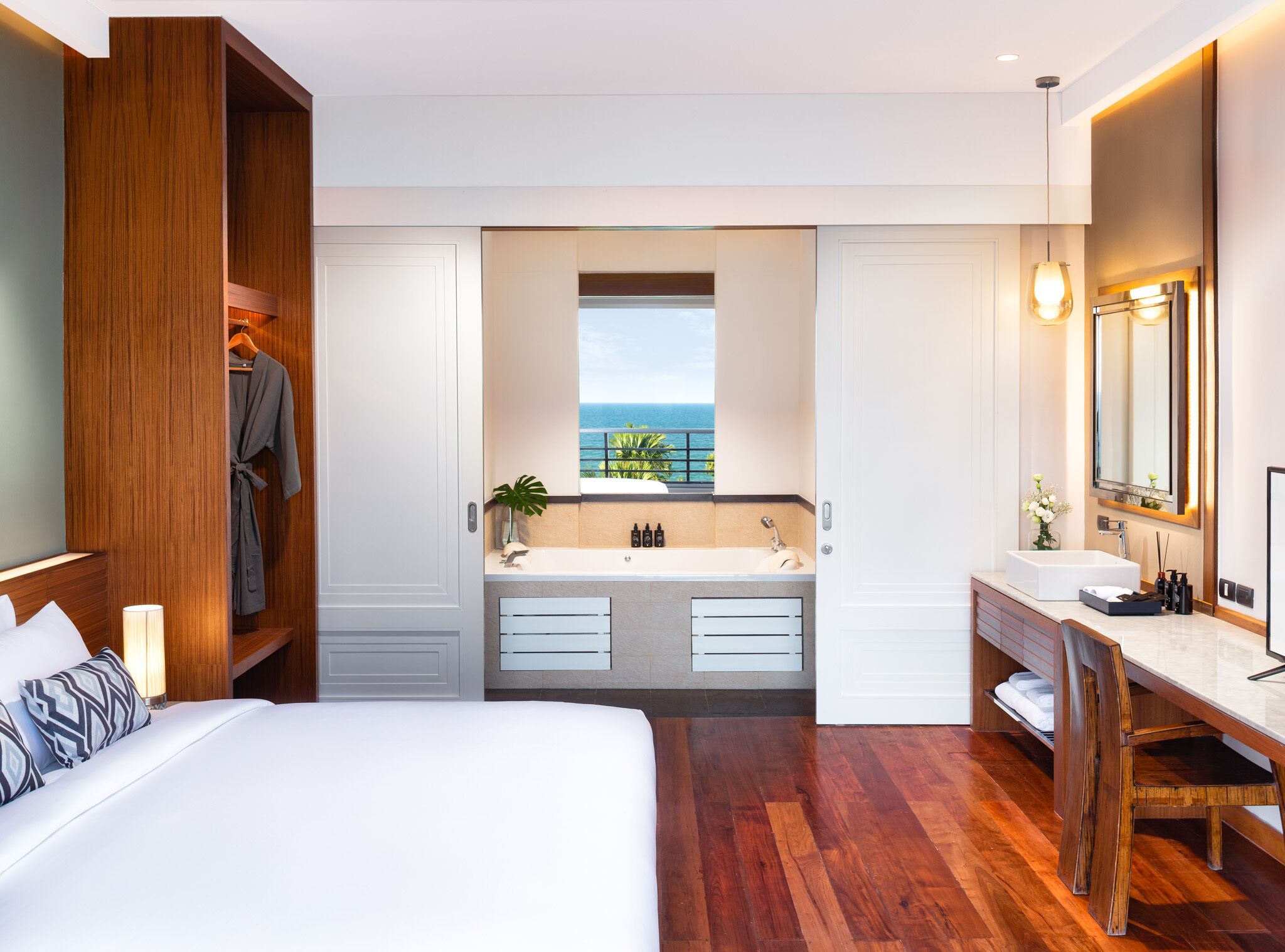 Una habitación de hotel moderna con una cama grande, un baño con vistas al océano y un armario de madera.