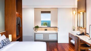 Una habitación de hotel moderna con una cama grande, un baño con vistas al océano y un armario de madera.