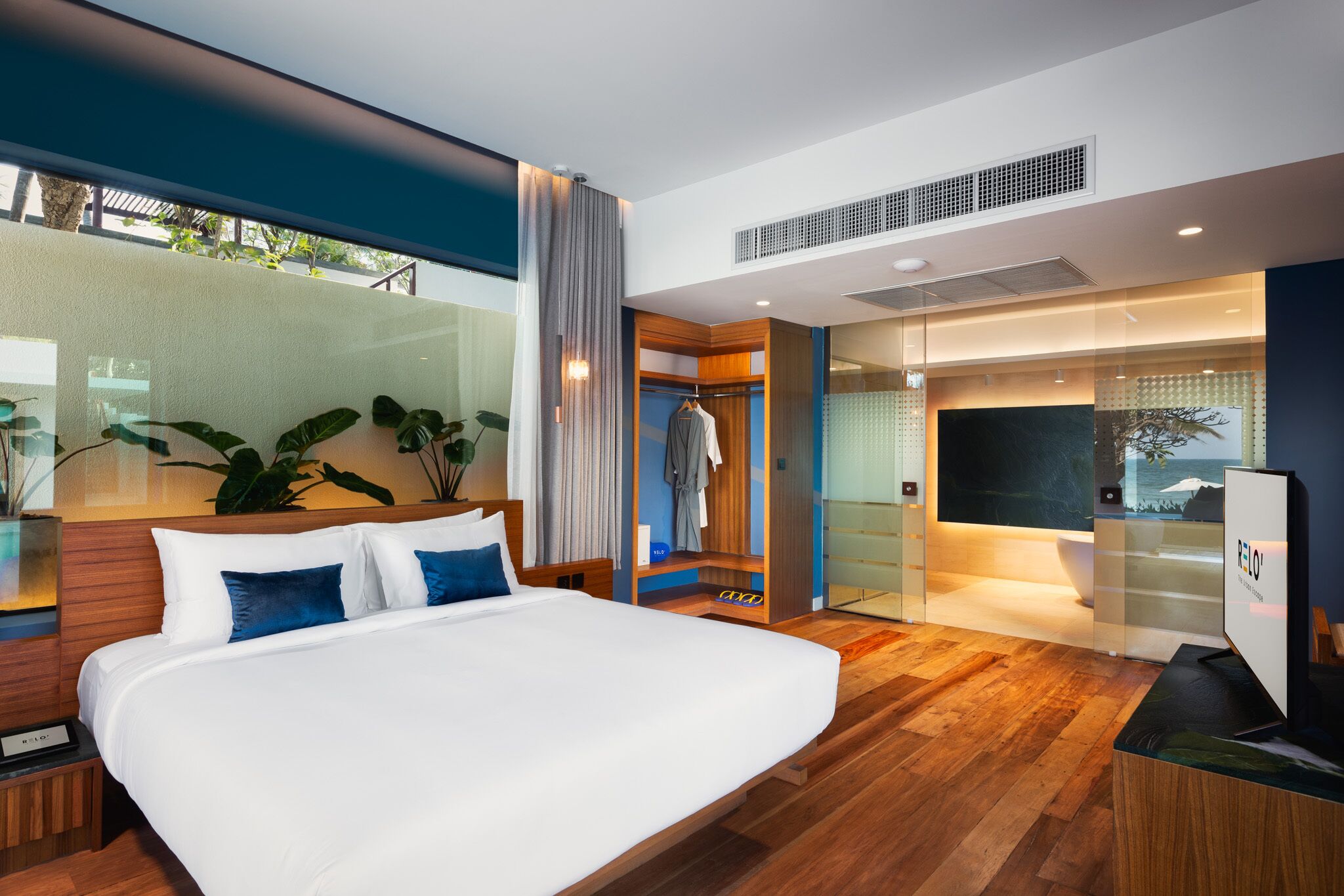 A modern hotel room with a large bed, a walk-in closet, a TV, and a view of the ocean.