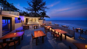 Un espacio exterior para comer con mesas y sillas, un bar y vistas al océano.