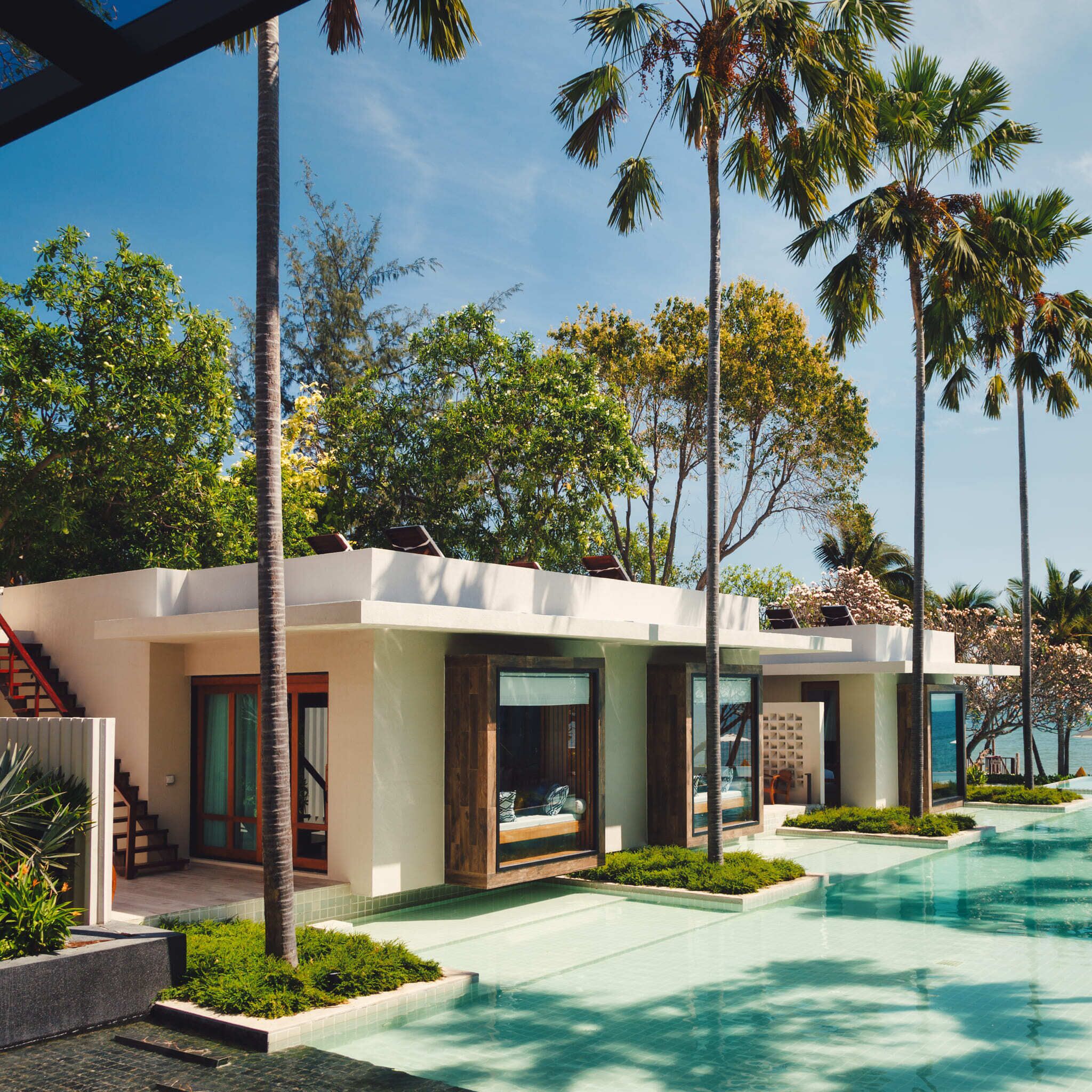 A modern resort with a pool, palm trees, and a clear view of the ocean.