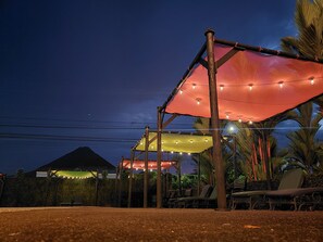 An outdoor seating area with a canopy structure, lounge chairs, and a mountain in the background.