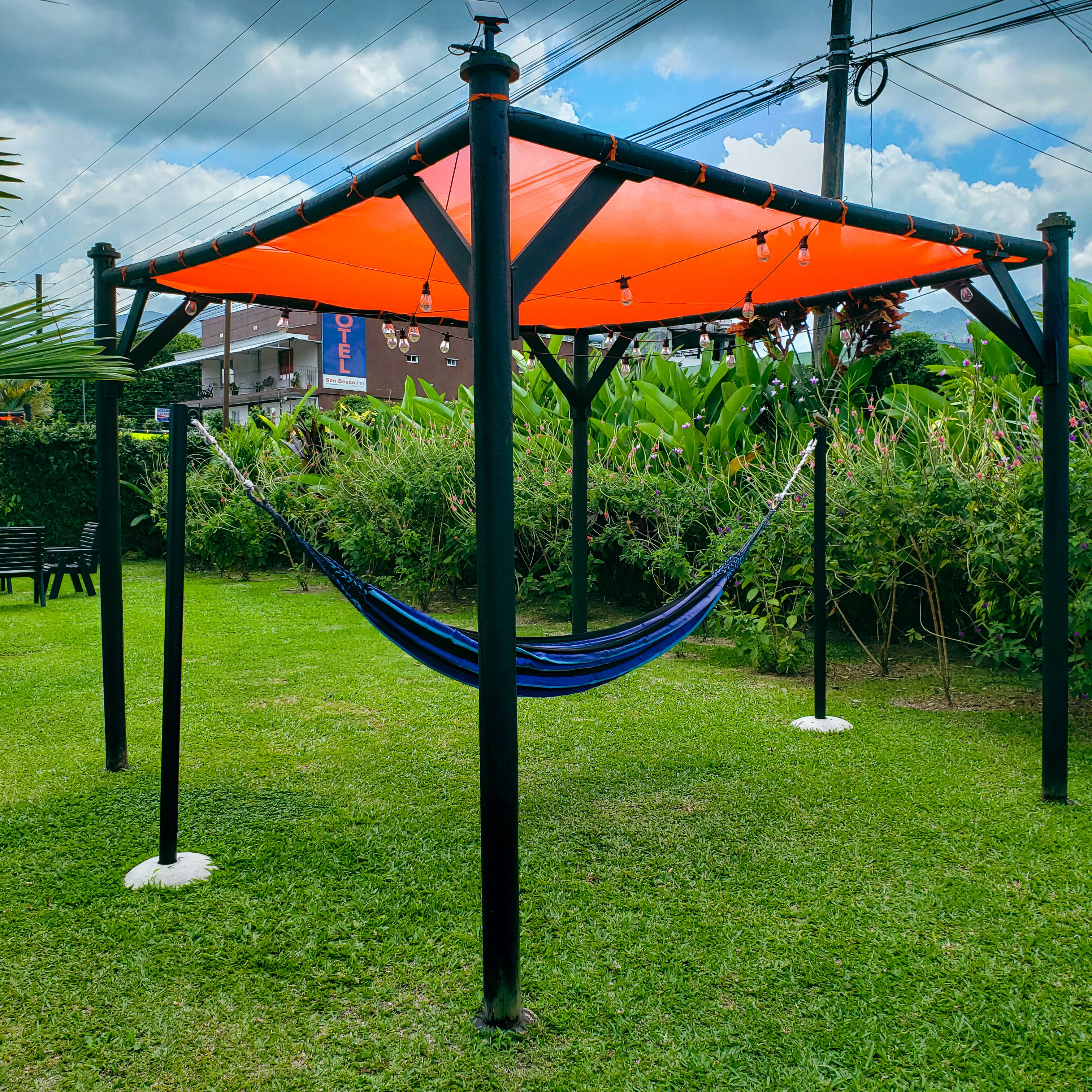 A hammock under an orange canopy in a grassy area with a building in the background.