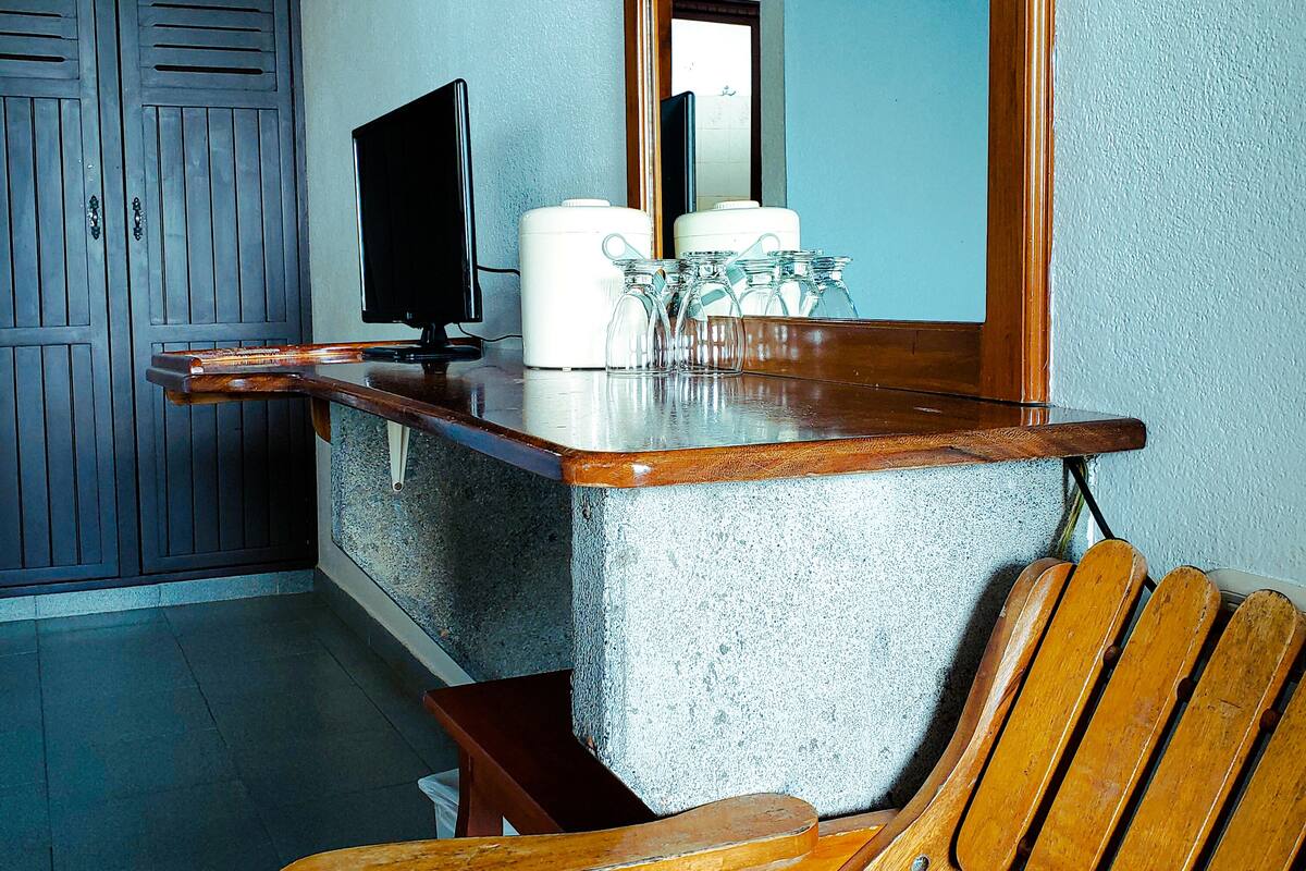 A room with a wooden chair, a television on a stand, and a mirror reflecting a window.