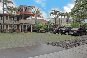 Un edificio de varios pisos con fachada de piedra, un espacio cubierto al aire libre y coches aparcados.