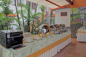 A buffet setup with a coffee machine, various food containers, and a mural on the wall.