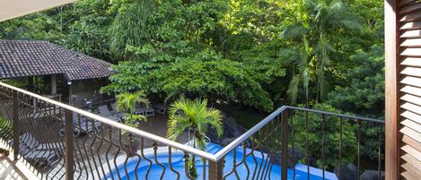 Un balcone con vista su una piscina circondata da vegetazione lussureggiante.