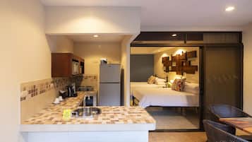 Una habitación de hotel compacta con kitchenette, una cama con almohadas y un comedor con sillas de mimbre.