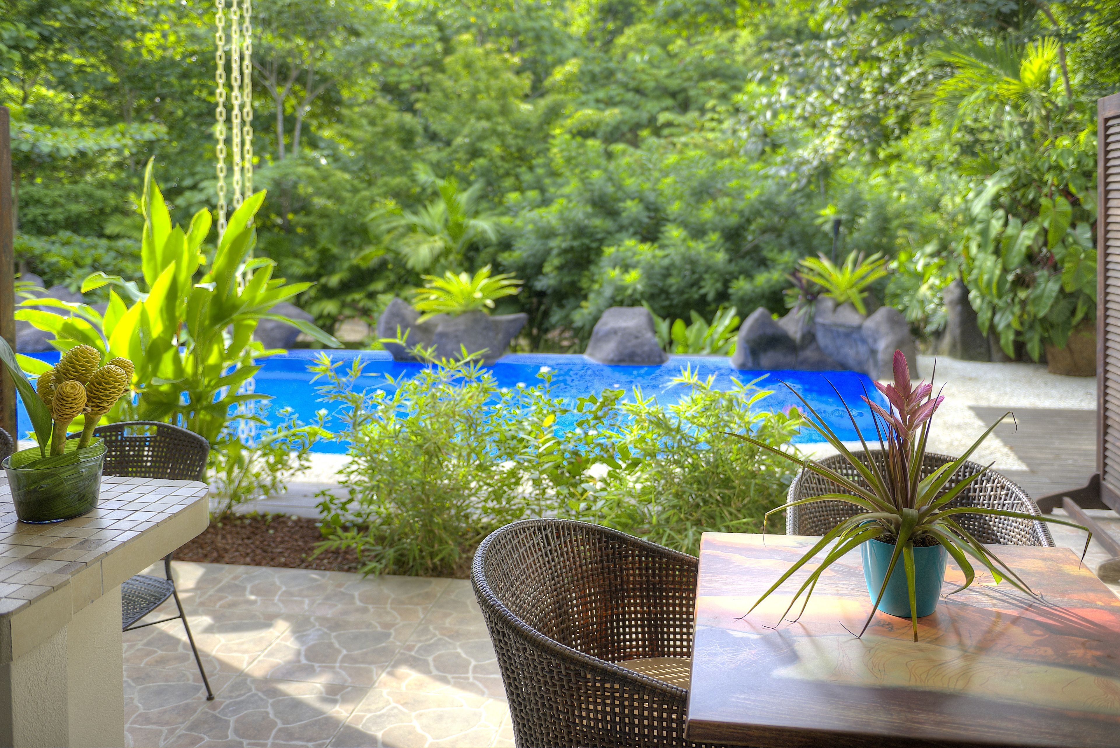 An outdoor seating area with a pool, surrounded by lush greenery and rocks.