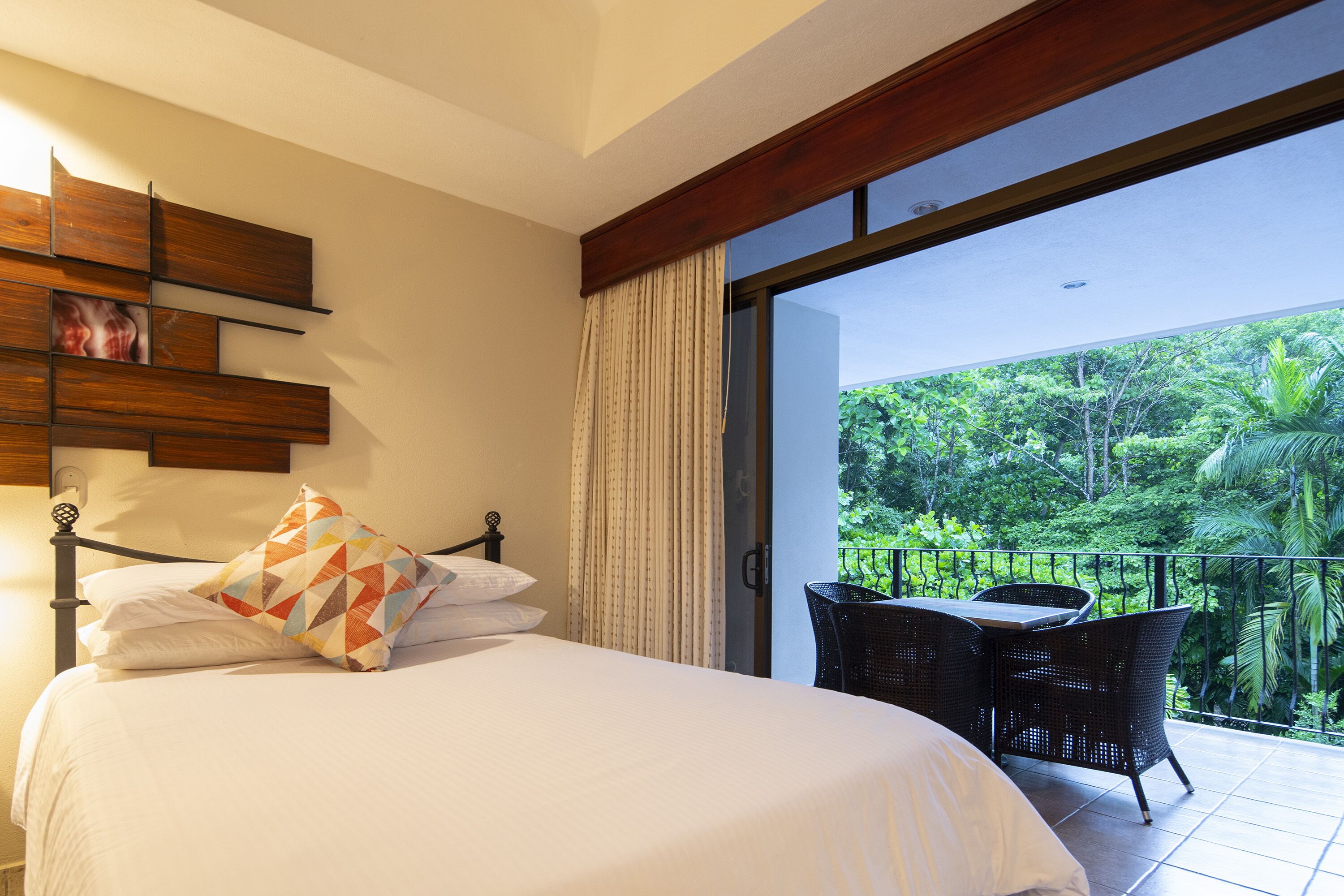 A bedroom with a bed, a wooden shelf, and a view of a balcony with outdoor furniture.
