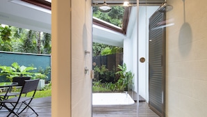 Uma casa de banho moderna com porta de vidro que dá para uma área exterior privada, chuveiro e um espaço de estar pequeno com mesa e cadeiras.