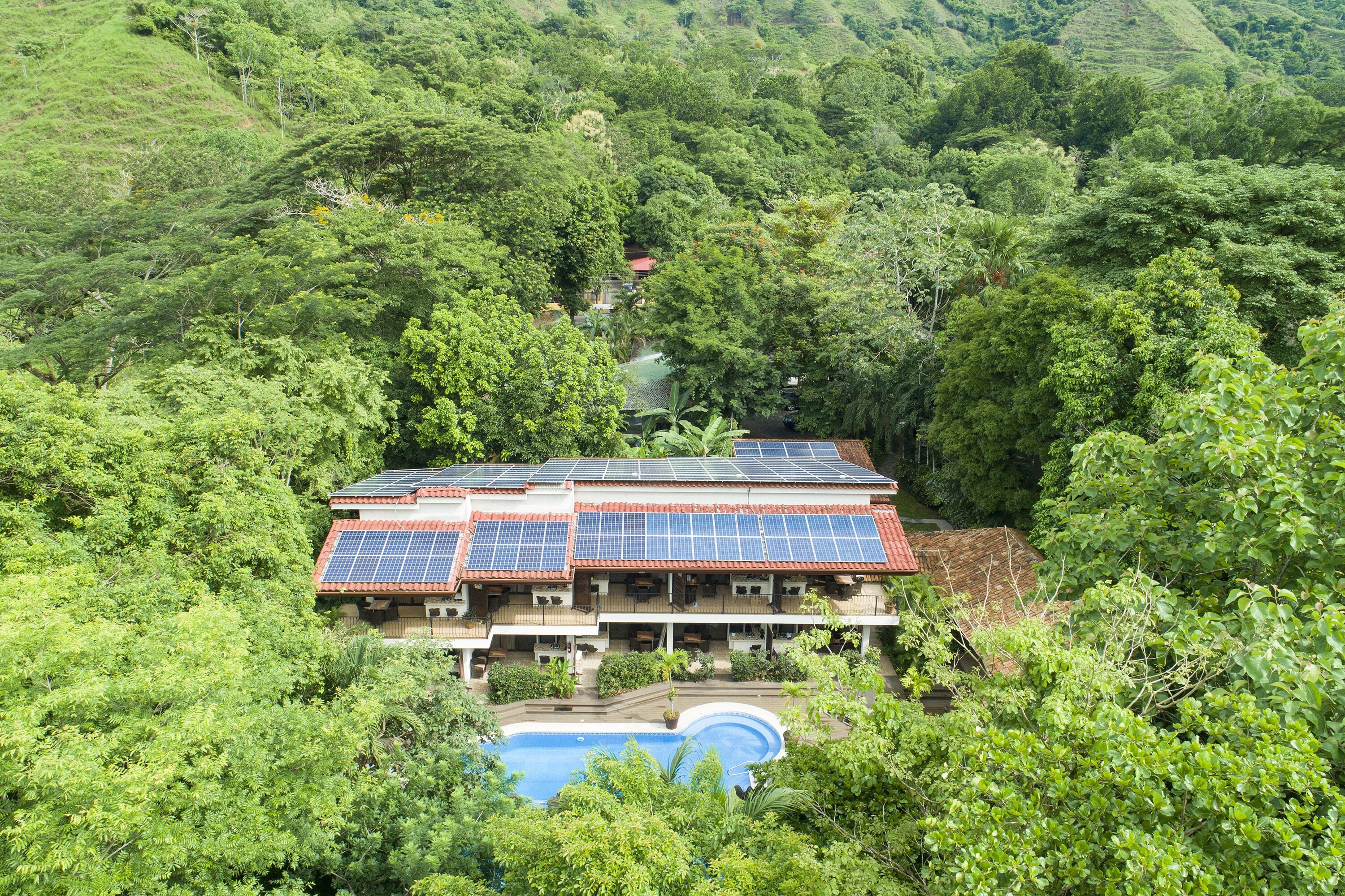 A house with solar panels, a swimming pool, and lush greenery surrounding it.