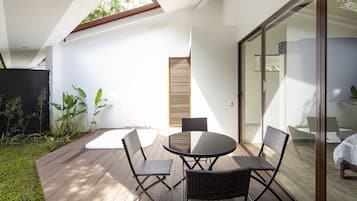 Een modern terras buiten met een ronde tafel en vier stoelen, omringd door een houten terras en een glazen deur die naar een binnenruimte leidt.
