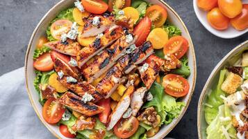 A bowl of salad with grilled chicken, tomatoes, and cheese.