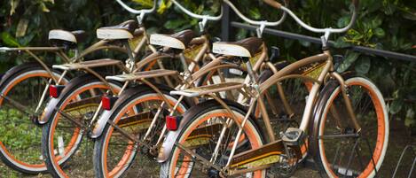 A row of vintage bicycles with orange rims and brown frames, parked against a metal railing with greenery in the background.