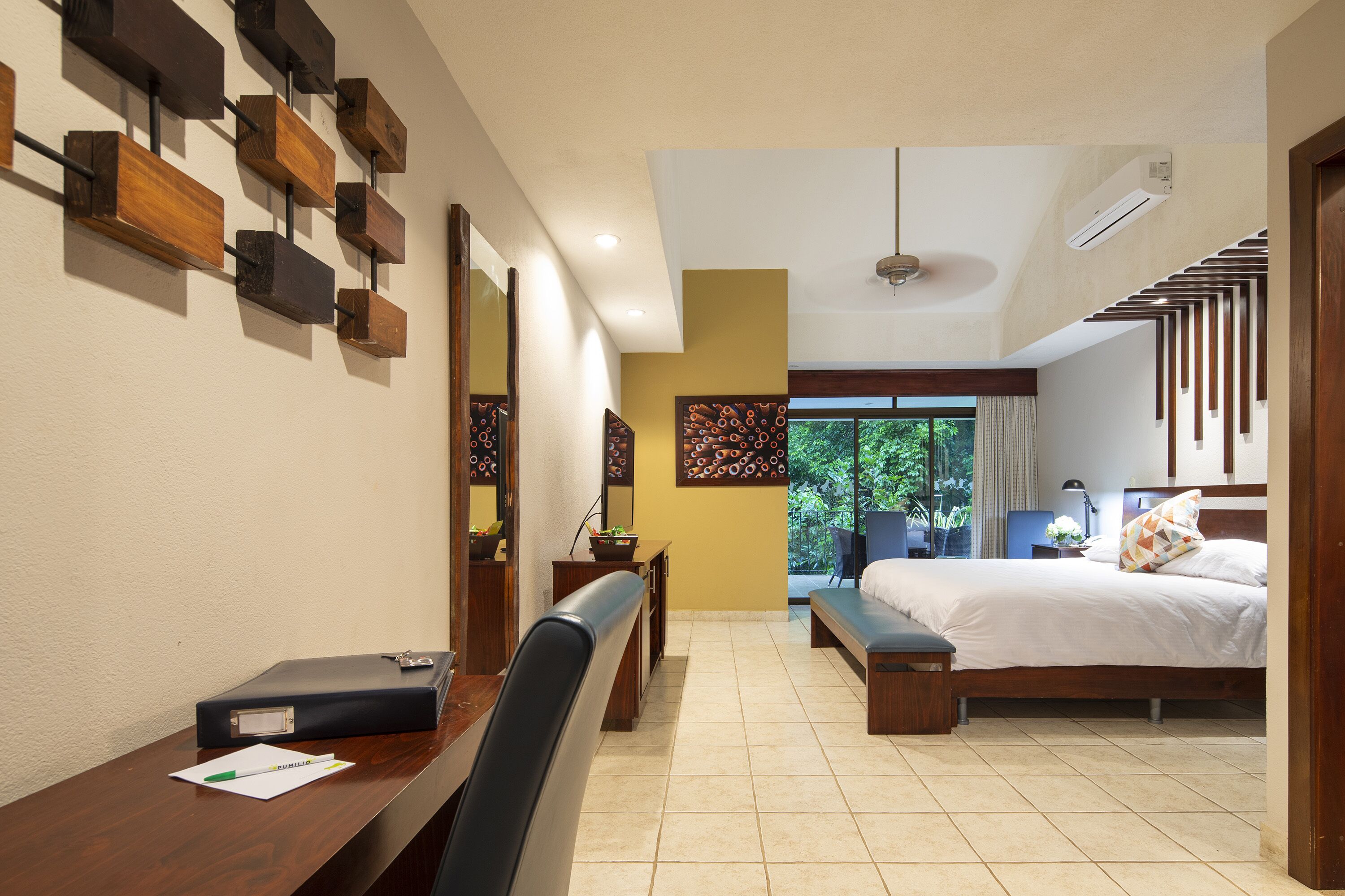 A hotel room with a desk, bed, and a view of greenery outside.