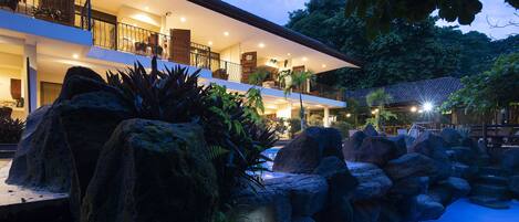A modern hotel with multiple balconies, a swimming pool, and lush landscaping.