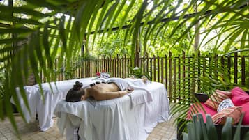 A spa area with two massage tables covered in white linens, surrounded by lush green foliage and a wooden fence.