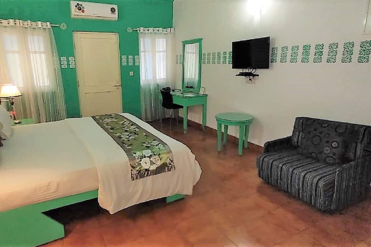 Una habitación con cama, escritorio, silla, televisor y espejo.