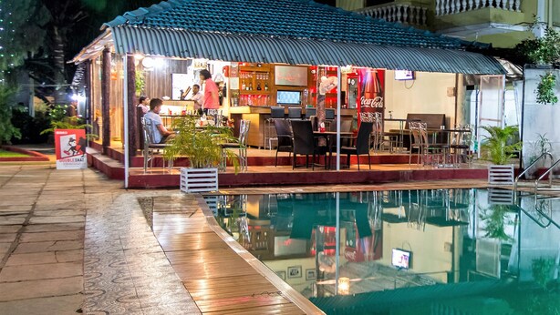 A poolside area with a covered seating area, a bar, and a Coca-Cola refrigerator.
