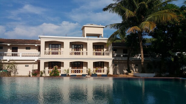 A two-story building with balconies, a swimming pool, and palm trees. - Hotel Riverside (Baga)