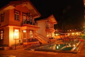 A hotel with a swimming pool, a staircase leading to the upper floor, and string lights around the pool area. - Tio Carmino (Calangute)