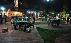 An outdoor dining area with tables and chairs, surrounded by a low wall and a grassy area. - Tio Carmino (Calangute)