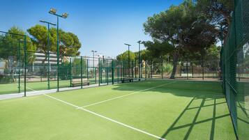 A tennis court with green artificial turf, surrounded by a green fence and trees.