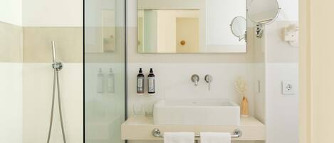 A modern bathroom with a glass-enclosed shower, a white sink with two bottles of shampoo, and a mirror above the sink.