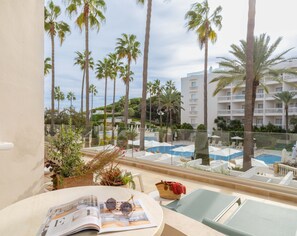 Un balcon avec un magazine, des lunettes de soleil et un sac à main. On aperçoit des chaises longues et une piscine à l’arrière-plan.