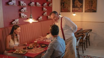 A restaurant with a red booth seating area, wooden chairs, and a wall decorated with shoe displays.