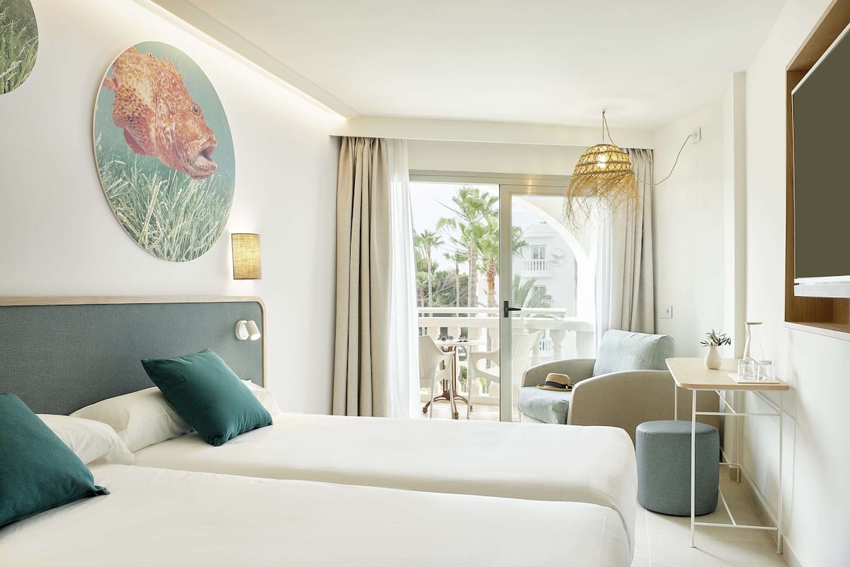 A hotel room with two beds, a balcony with a table and chairs, and a view of palm trees.