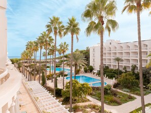 Un complexe hôtelier doté d’une piscine entourée de palmiers, d’un bâtiment blanc avec des balcons et offrant une vue dégagée sur l’océan.