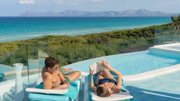 Zona de piscina con dos sillones reclinables, barandilla de cristal y vistas al océano y montañas.