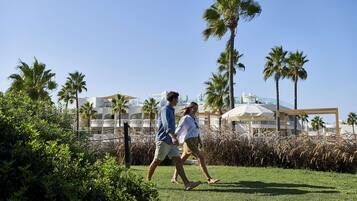 Una pareja caminando sobre un césped con palmeras y un edificio al fondo.