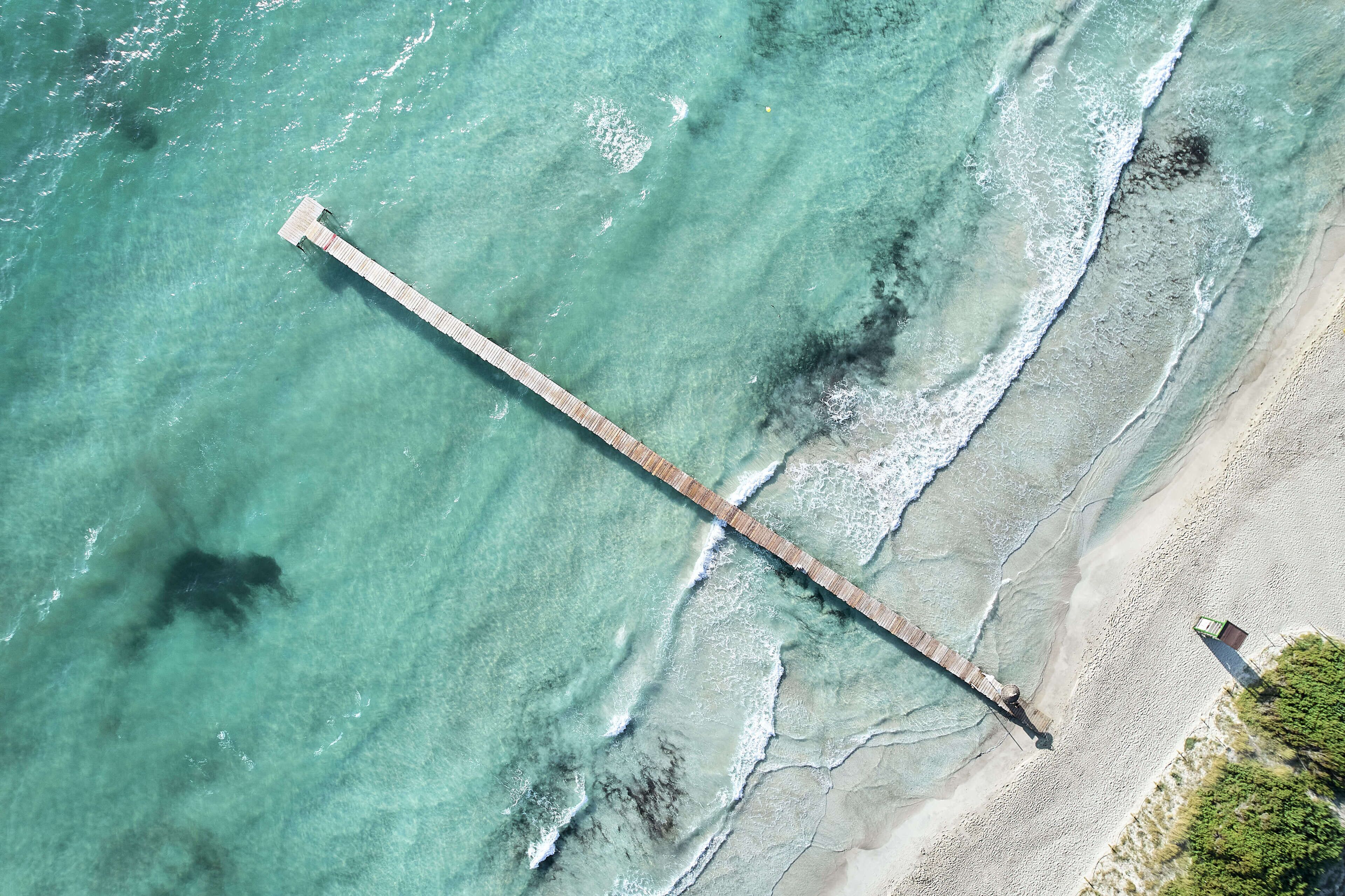 An aerial view of a beach with a long pier extending into the water.