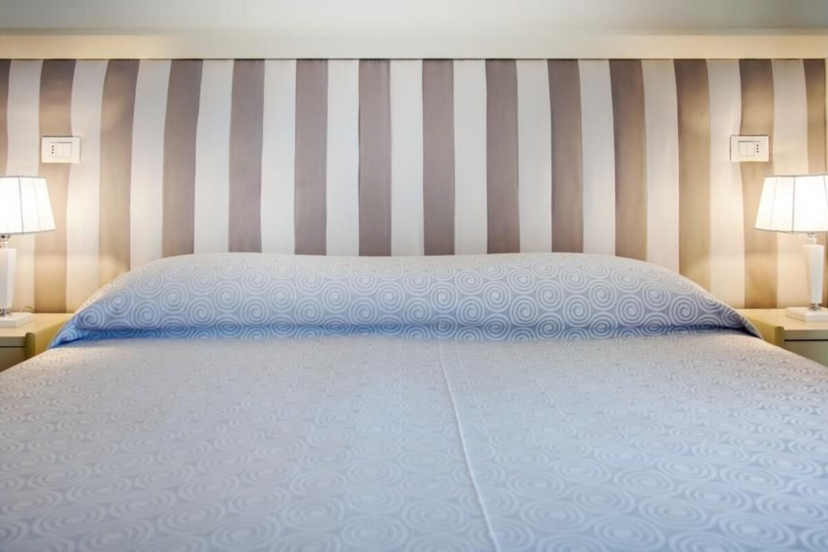 Habitació d'hotel amb capçaleri amb ratlles, dues làmpades de nit i un llençol estampat.