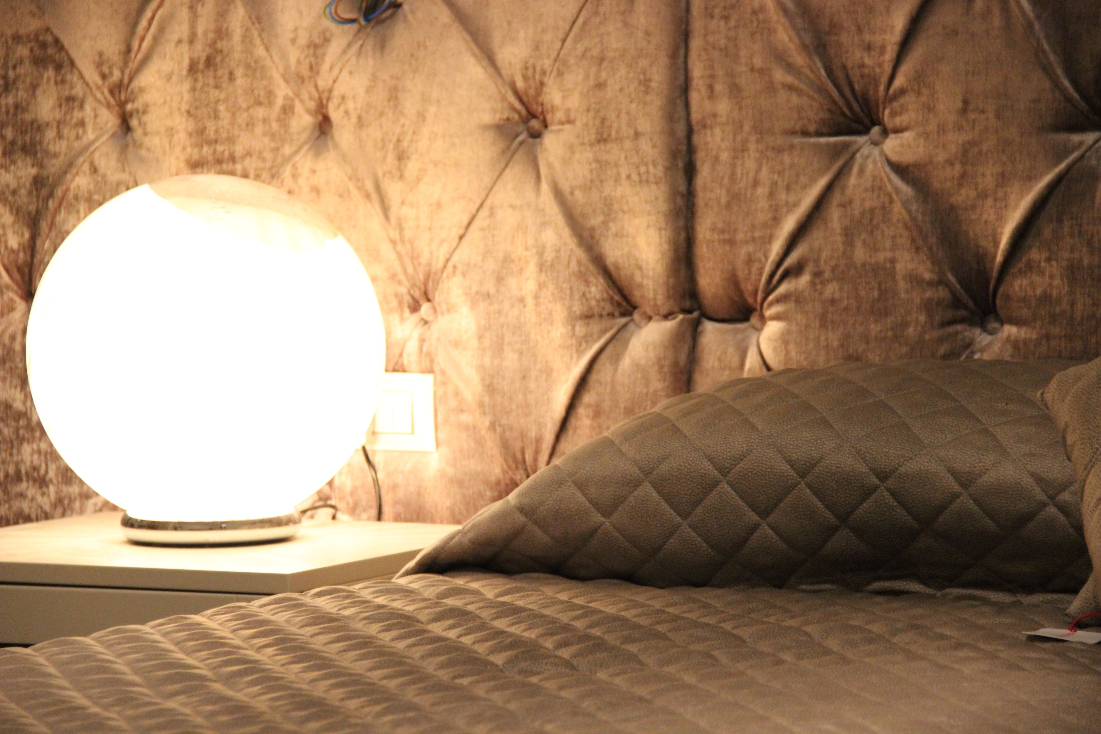 A tufted headboard, a round bedside lamp, and a quilted pillow on a bed.