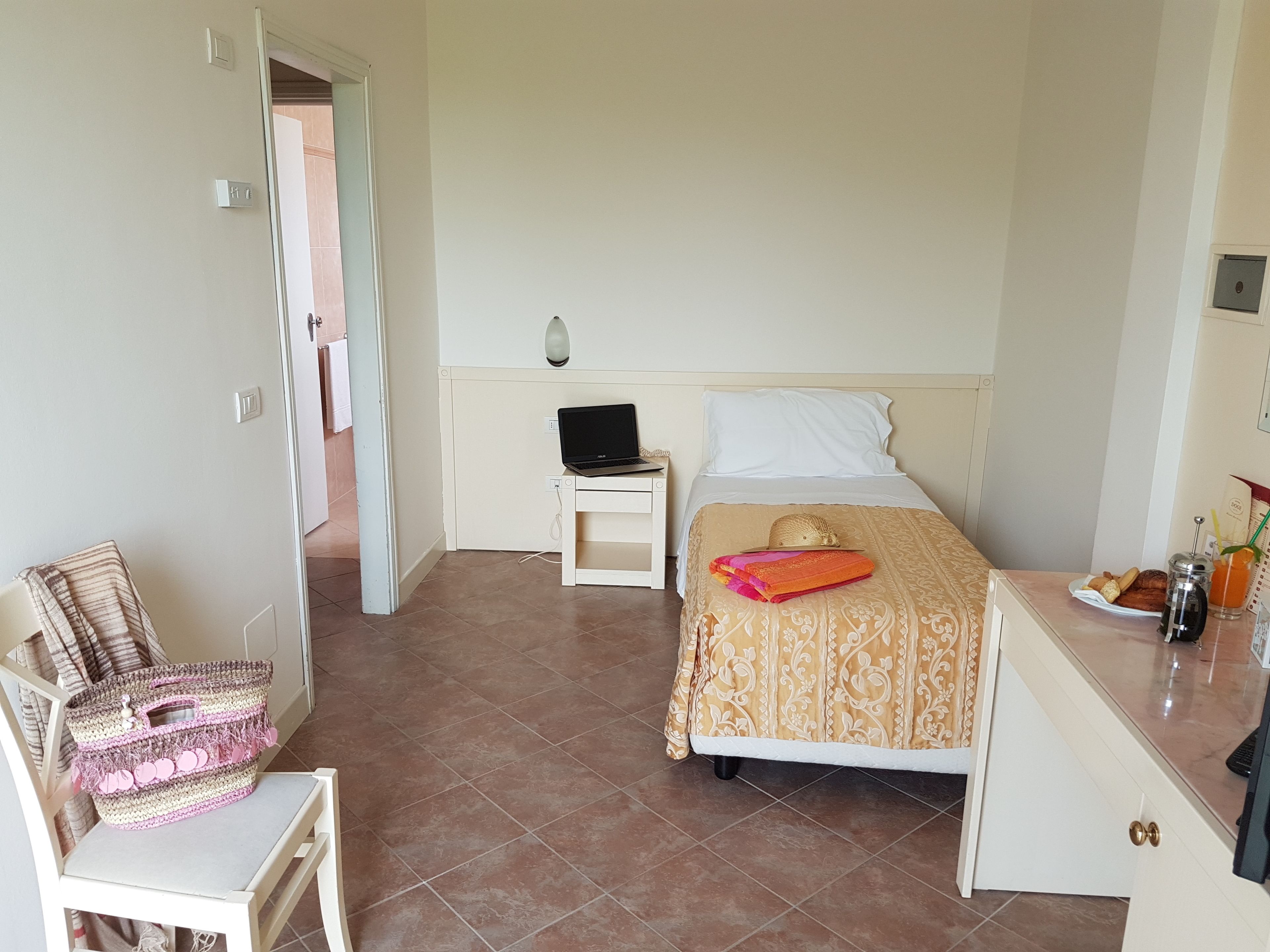 A bedroom with a bed, a desk, a chair, and a laptop on a nightstand.