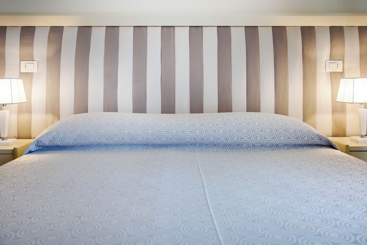 Una habitación de hotel con un cabecero a rayas, dos lámparas de noche y una colcha estampada.