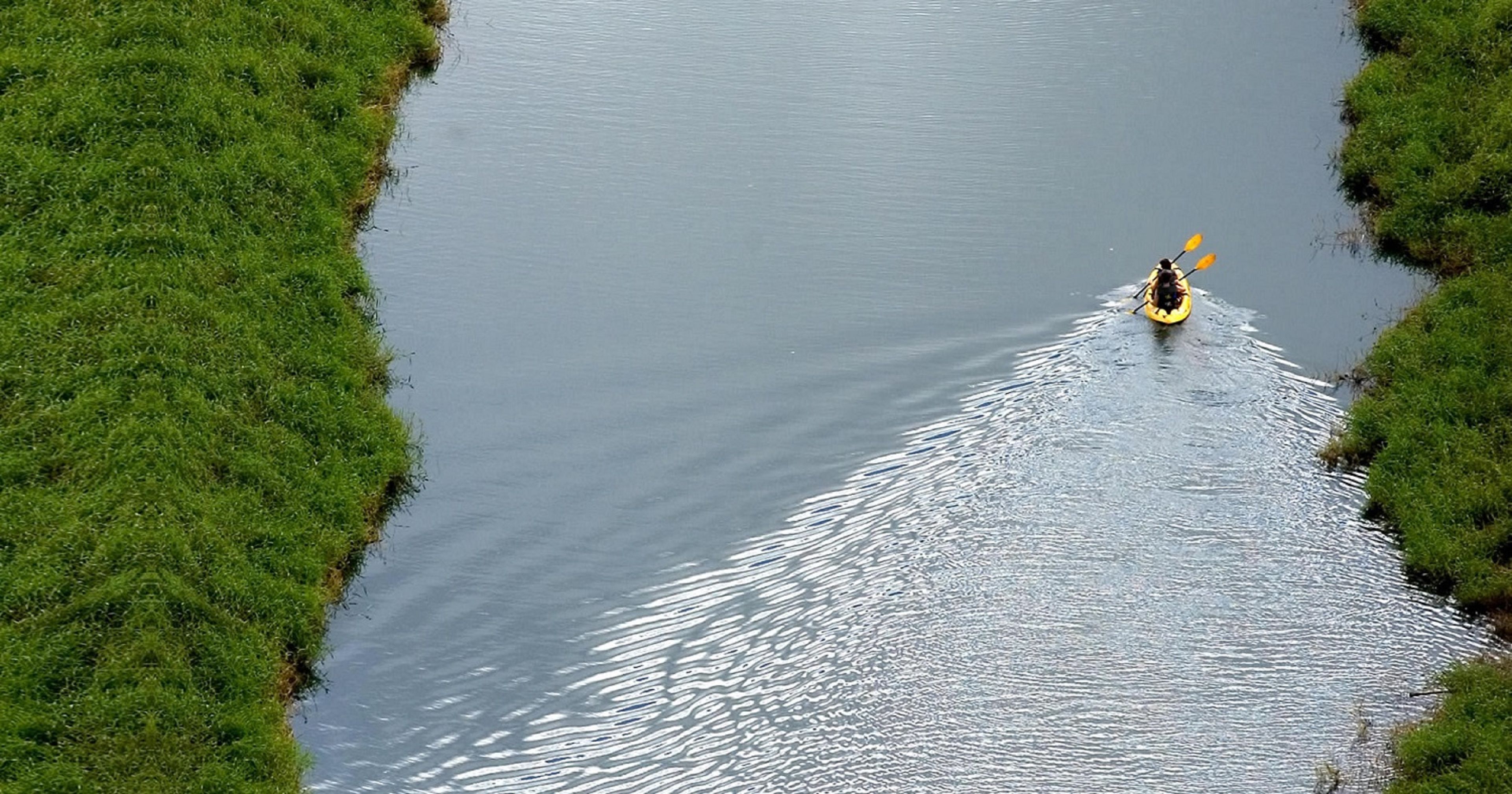 A kayaker in a narrow water channel surrounded by lush green banks.