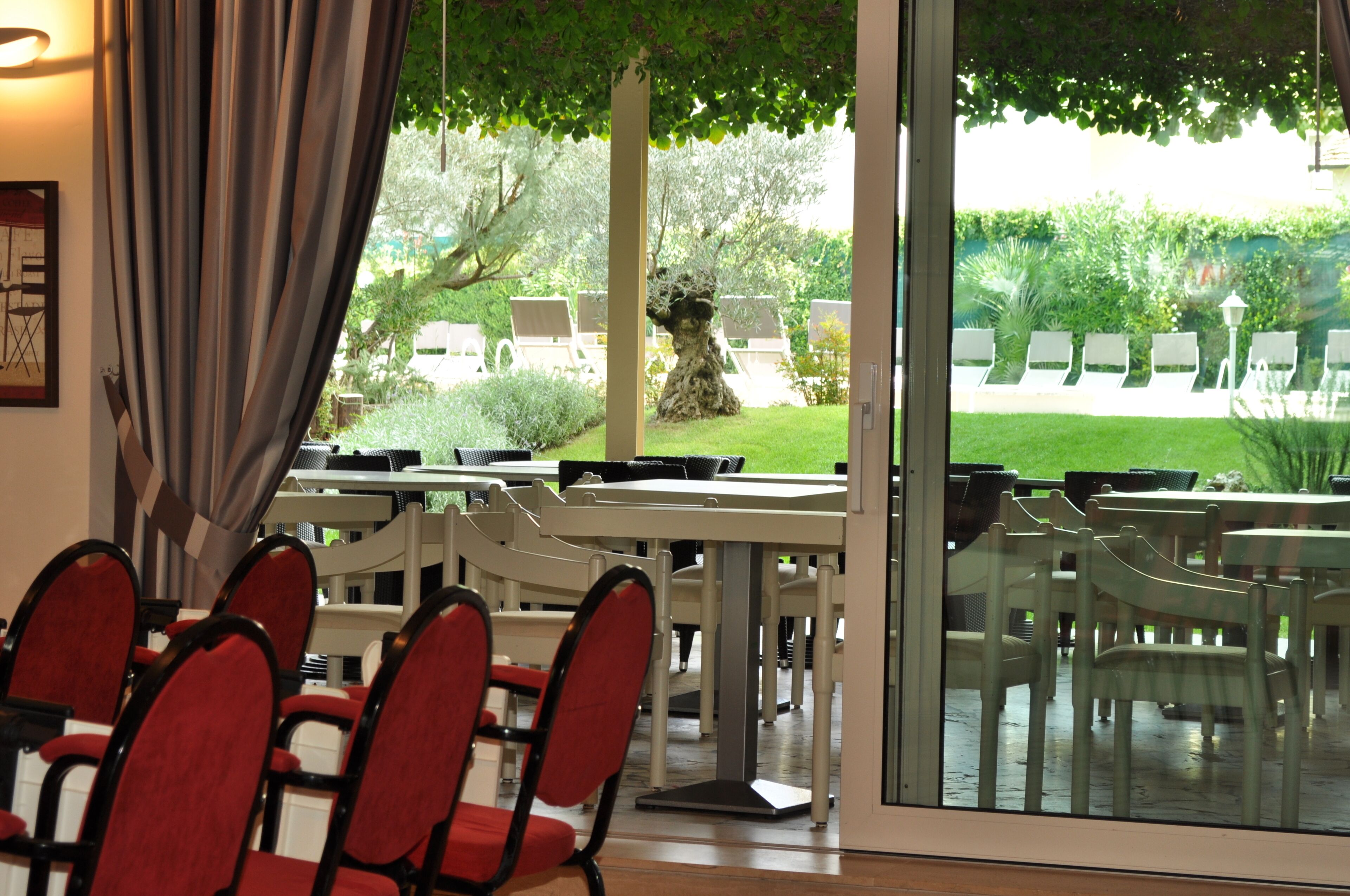 Un ristorante con posti a sedere interni, vista sul giardino e un'ampia finestra con tende.