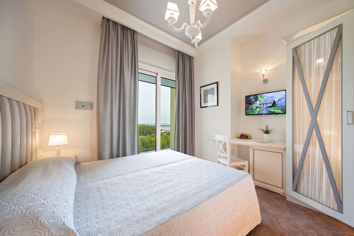 Hotellihuone, jossa on sänky, työpöytä, televisio ja näkymä vihreälle alueelle.