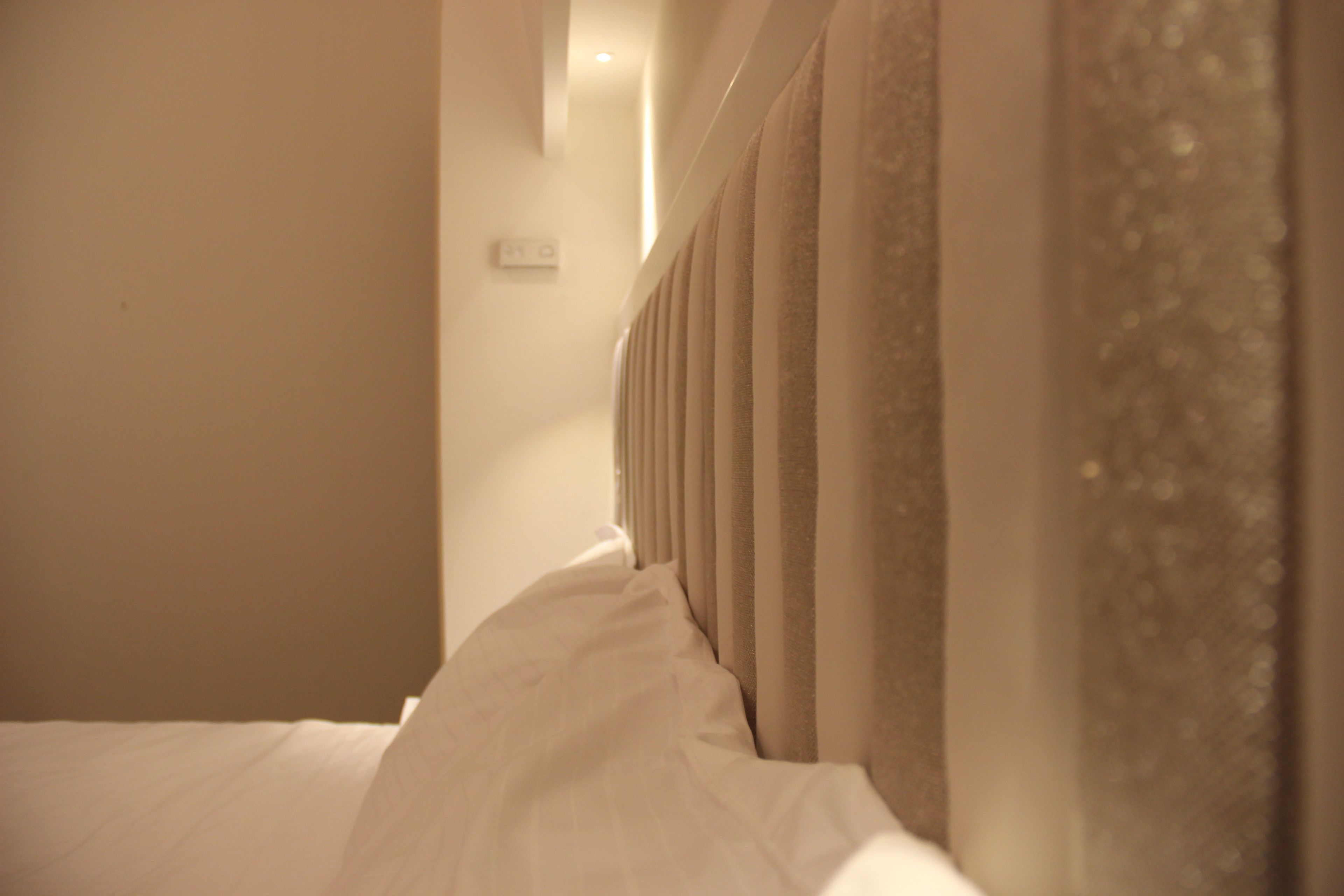 A hotel room with a bed, curtains, and a wall-mounted light fixture.